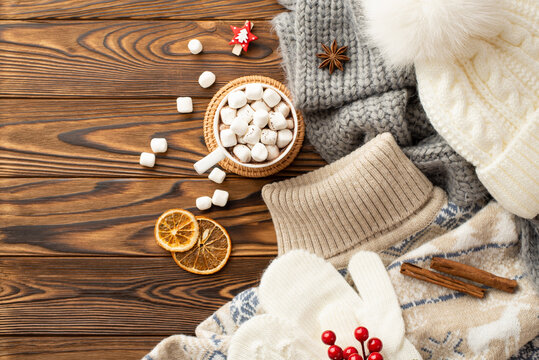 Top view photo of pullover headwear plaid mittens cup of cocoa with marshmallow on rattan placemat decorative clip dried orange slices viburnum berries cinnamon sticks anise on wooden table background