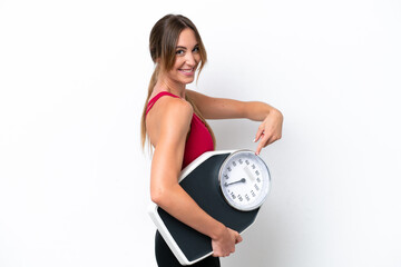Young caucasian woman isolated on white background holding a weighing machine and pointing it