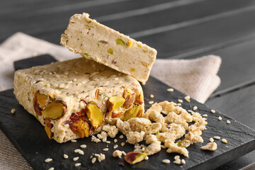 Board of tasty sesame halva with pistachios on dark wooden table, closeup