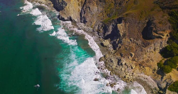 Aquamarine waters of Pacific Ocean meeting rugged craggy rocks of the California coast. Amazing white waves at Morro Bay from aerial view.