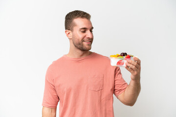 Young caucasian man holding a bowl of fruit isolated on white background with happy expression