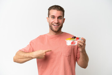 Young caucasian man holding a bowl of fruit isolated on white background with surprise facial expression