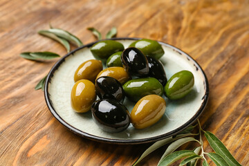 Plate with delicious olives on wooden background