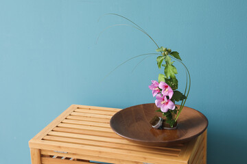 Bowl with beautiful ikebana and kenzans on wooden table near blue wall