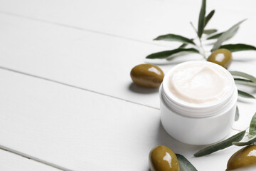 Fototapeta na wymiar Jar of cream with green olives and plant branch on white wooden background, closeup