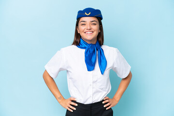 Airplane stewardess caucasian woman isolated on blue background posing with arms at hip and smiling