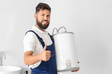 Male plumber with boiler showing thumb-up in bathroom