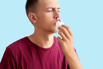 Young man wiping nosebleed with tissue on blue background