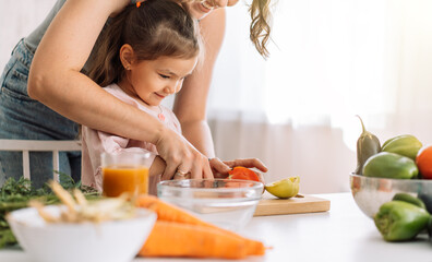 Obraz na płótnie Canvas Mom and daughter cook food together slicing tomato.