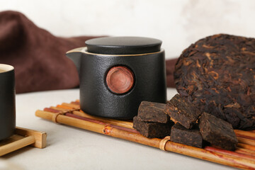 Bamboo mat with dry pressed puer tea and teapot on white background, closeup