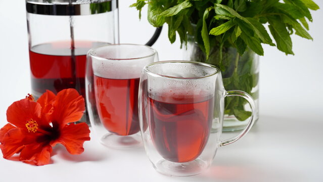 Two transparent glasses a with hot red carcade floral tea