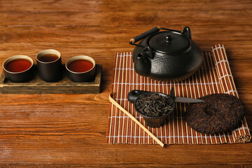 Dry pressed puer tea, teapot and cups of hot beverage on wooden table