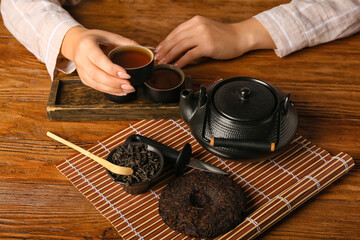 Fototapeta na wymiar Female hands with cup of aromatic puer tea on wooden background
