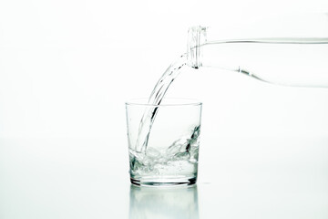 Glass bottle pouring water in a glass over a white background