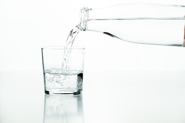 Glass bottle pouring water into a half-full glass on a white background.