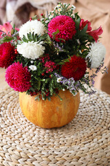 Pumpkin with beautiful flowers on rattan pouf in bedroom, closeup