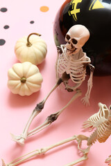 Skeletons and pumpkins for Halloween party on pink background, closeup