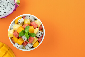 Fruit salad with mango, watermelon, dragon fruit, pineapple, mint on orange background. Top view, copy space.