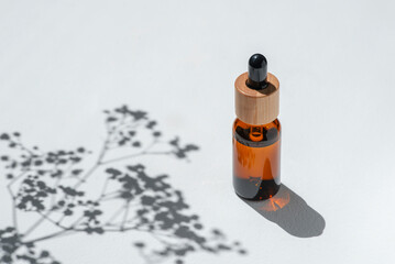 Amber bottle with cap with serum or essential oil with flowers shadows. White background with...