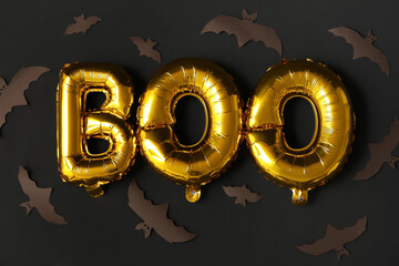 Word BOO made of foil balloons and paper bats on dark background