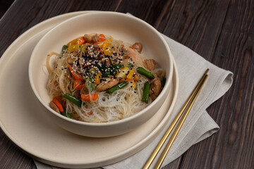 Funchoza wok with chicken, carrots, sweet peppers and beans in a deep beige plate, metal sticks on a napkin, open space