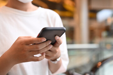 Woman hands typing message on smart phone, standing on blurred background of shopping mall and escalator