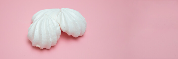 White meringues on pink background. French dessert prepared from whipped with sugar and baked egg whites. Greeting card with copy space
