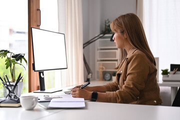 Side view of focused female entrepreneur working online with computer in her home office