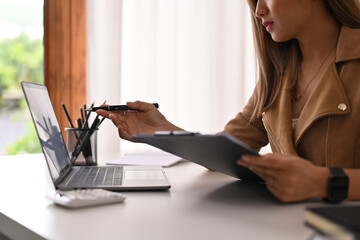 Cropped shot of female investor holding clipboard and pointing on laptop computer screen