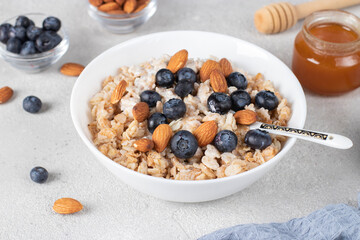 Oatmeal porridge with blueberries, almonds and honey on light gray background. Breakfast meal concept
