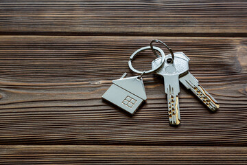 Keys with a keychain in the form of a house lie on an old wooden table. The concept of buying, renting, home insurance. Real estate transactions. Space for text.