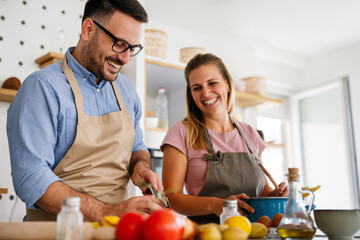 Young happy couple is enjoying and preparing healthy meal in their kitchen together