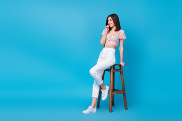 Full length photo of sweet lady sit comfy hair look interested empty space bite fingernail date weekend isolated on blue color background