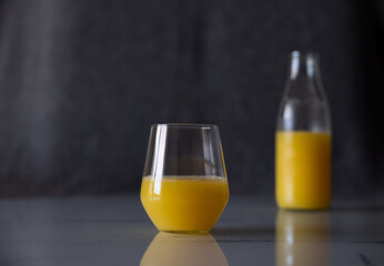 A glass of orange juice on the table. In the background, not a full bottle of juice is out of focus.