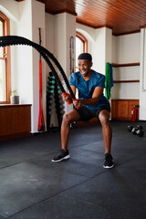 Fototapeta na wymiar Young black man doing intense cardio workout with battle ropes at the gym