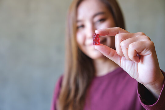 Blurred image of a young woman holding and looking at a red jelly gummy bear
