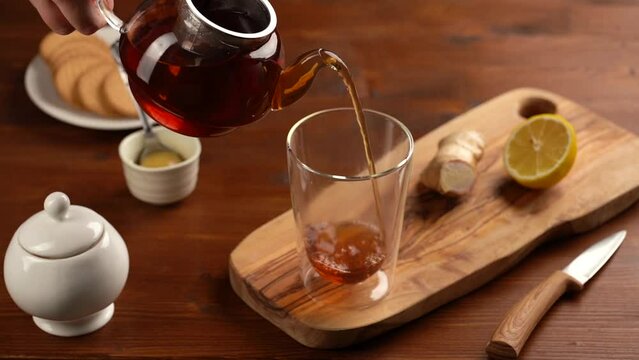 Pouring black tea into transparent coffee glass with black coffee on wooden board on wooden brown table
