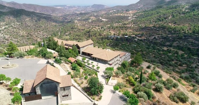 Aerial drone footage of Holy monastery of Panagia Amirous in Apsiou, Limassol, Cyprus. Reveal scene of the religious stone church, ceramic roof tiles and surrounding mountain landscape from above