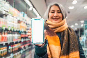 Senior woman at the supermarket shows the screen of her smartphone