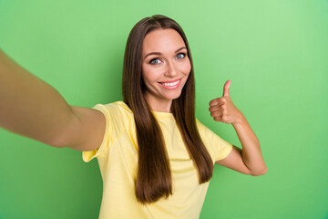 Fototapeta premium Photo of positive cheerful toothy beaming girl long hairstyle wear yellow t-shirt make selfie thumb up isolated on green color background