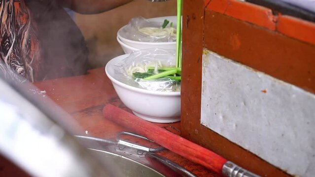 cooking street food named "Mie Ayam". Prepare chicken noodles. Indonesian cuisine. Selective focus on seller's hand and bowl. 4K videos.