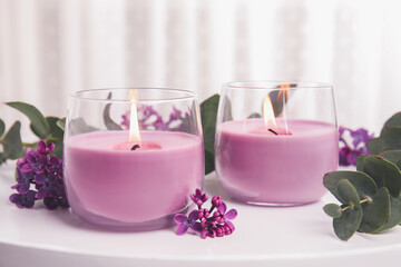 Fototapeta na wymiar Burning candles in glass holders and flowers with leaves on white table