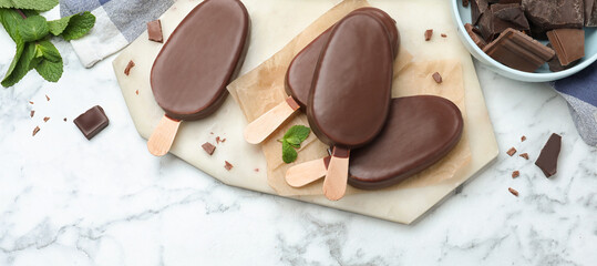 Delicious glazed ice cream bars with mint and chocolate on white marble table, flat lay. Banner...