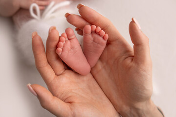 The palms of the parents. A mother hold the feet of a newborn child in a white blanket on a white background. The feet of a newborn in the hands of parents. Photo of foot, heels and toes.
