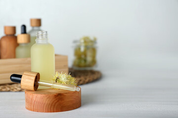 Fototapeta na wymiar Bottle of essential oil and linden flowers on white wooden table. Space for text