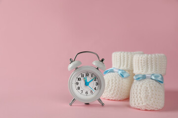 Alarm clock and baby booties on pink background, space for text. Time to give birth