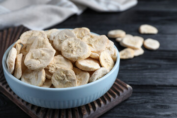 Bowl with dried banana slices on black wooden table, closeup