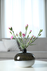 Fototapeta na wymiar Vase with beautiful carnation flowers on table in living room, space for text. Stylish element of interior design