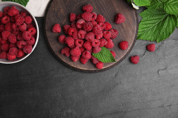 Fresh ripe raspberries with green leaves on black table, flat lay. Space for text