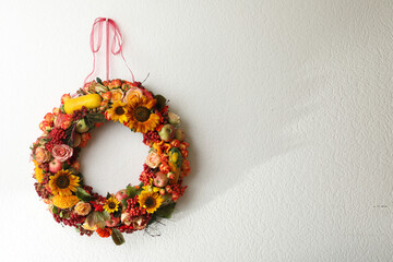 Beautiful autumnal wreath with flowers, berries and fruits hanging on white wall. Space for text - Powered by Adobe